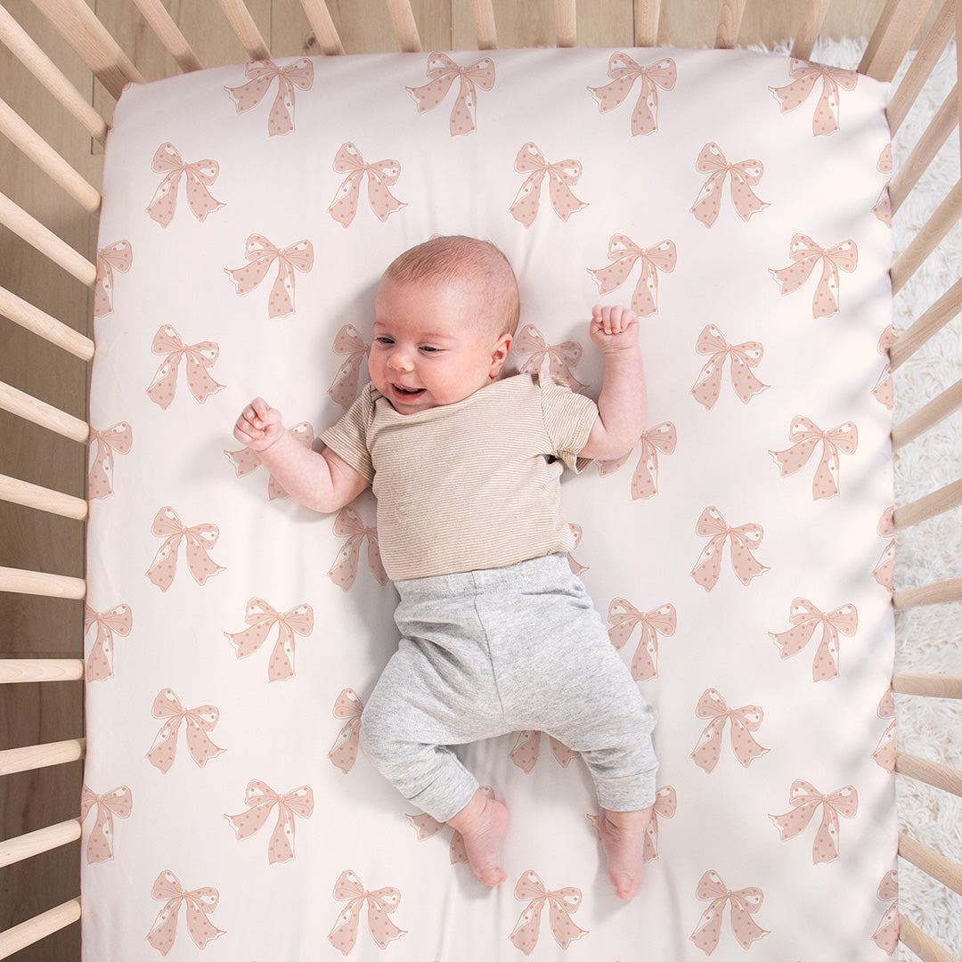 Baby lying on a crib with a bow-patterned sheet