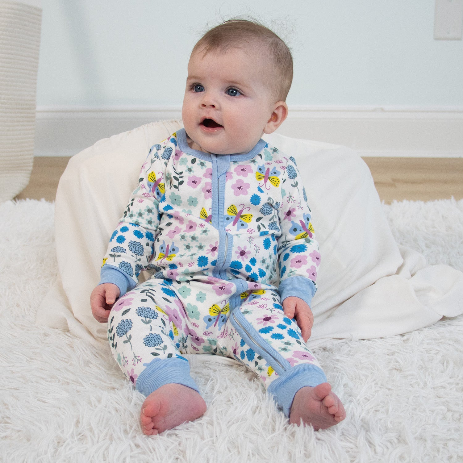 Baby wearing a floral onesie sitting on a white surface