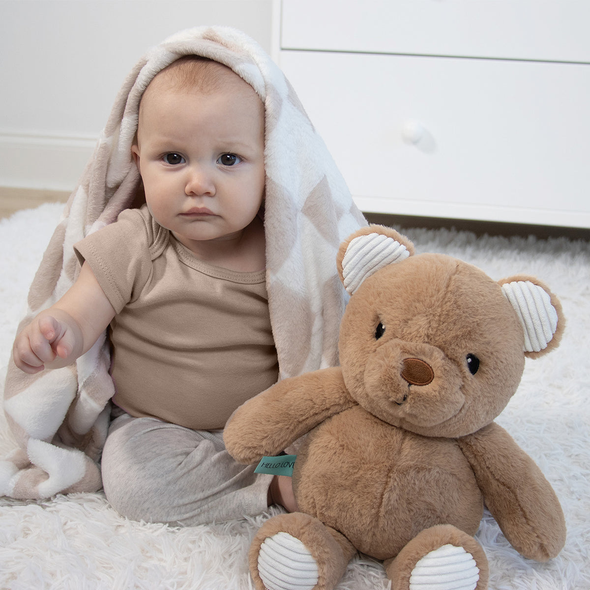 Baby wrapped in a blanket with a teddy bear on a light-colored surface